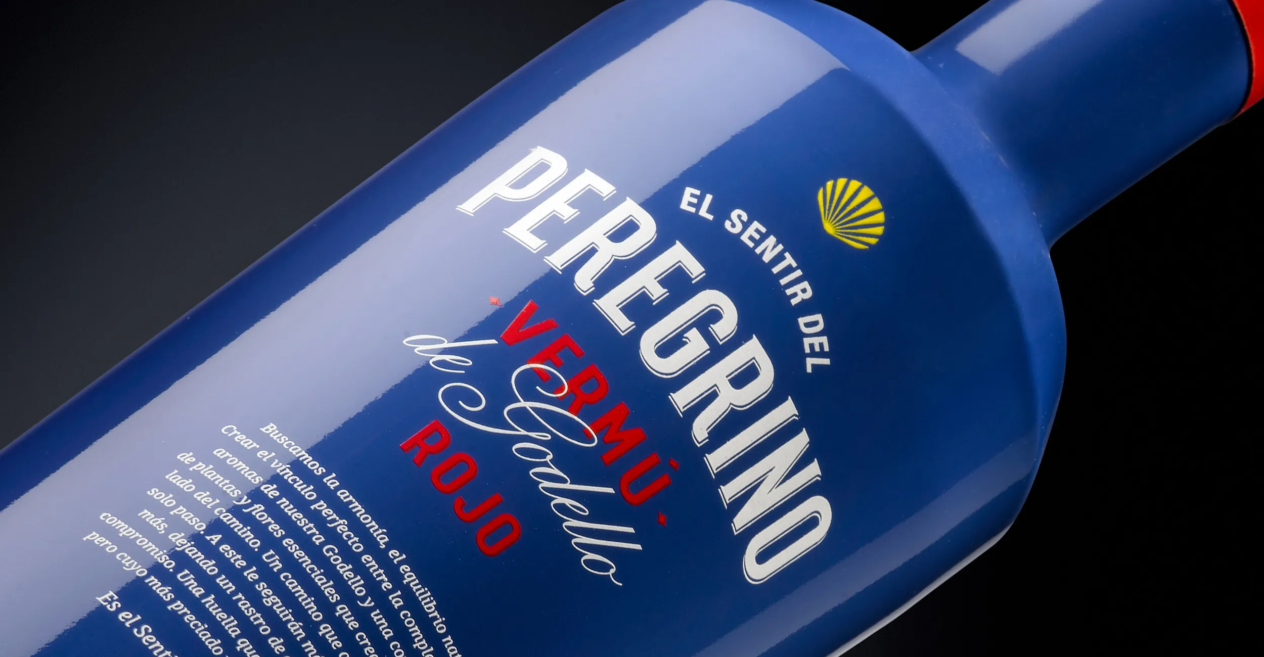 Etiqueta azul del vermut El Sentir del Peregrino, con tipografía blanca y roja y una concha amarilla del Camino de Santiago.